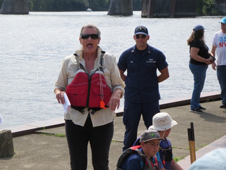 An Event Organizer Hollers Safety Instructions While The Coast Guard Heavy Stands Behind Her